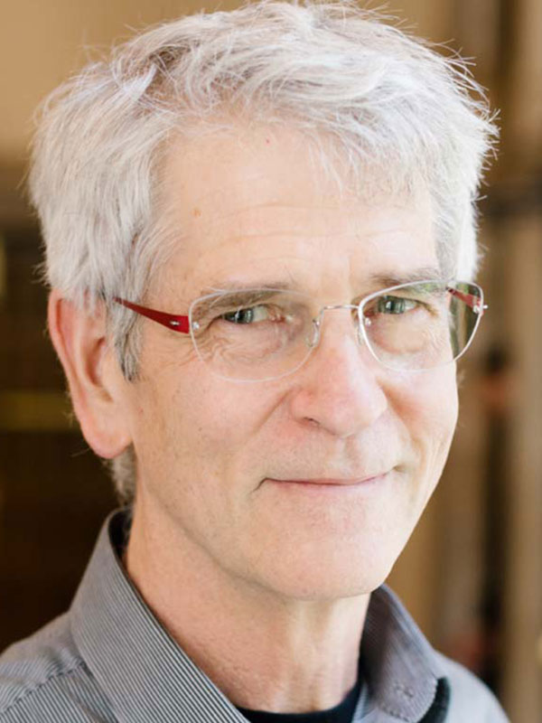 A headshot of Kirk Ludwig, who wears a striped gray dress shirt.