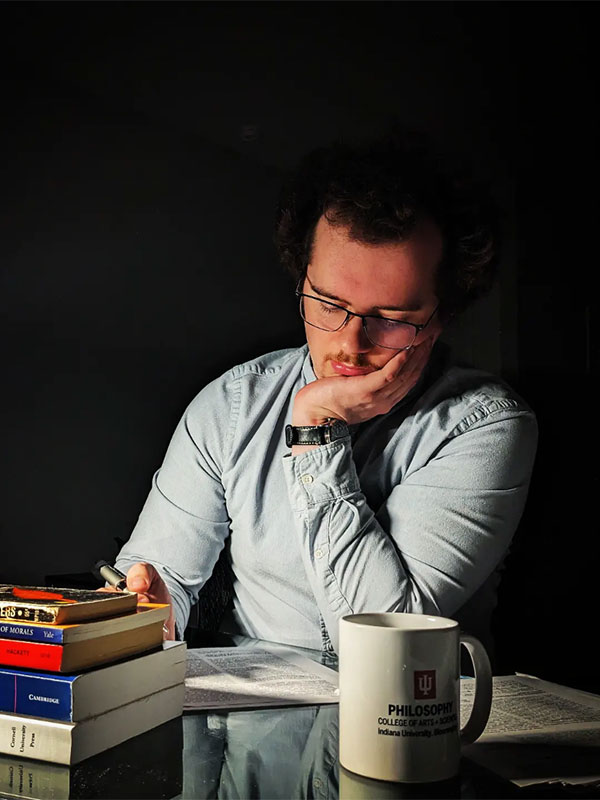 A photo of Eli Schantz, who poses at a desk while reading.